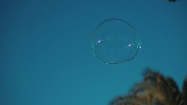 One Soap Bubble Flies in Blue Colour Sky Close up. Happy Playful Person with Foam Blower Enjoys Birthday Fun Outside in Summer Day. Outdoors Game with Bubbly Round Shape of Float Ball From Soapy Water