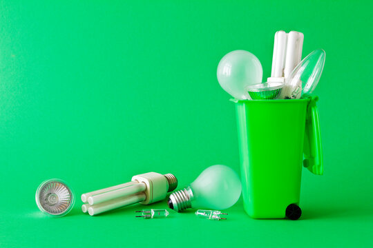 Stop Energy Waste Concept: Diverse Old Halogen And Fluorescent Light Bulbs In And Around A Recycling Bin, Green Background, Text Or Copy Space.