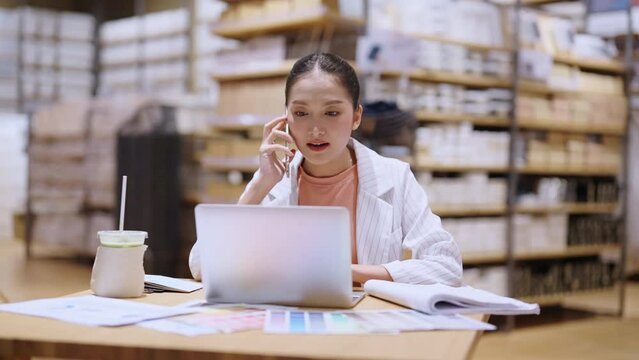 asian female smart entrepreneur working use laptop device stock manage and checking product inventory in warehouse showroom,asia woman smiling cheerful business owner work in showroom warehouse store