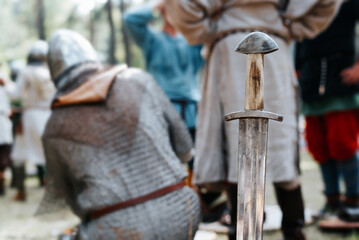 Medieval old steel sword against the background of knights outdoors. Close-up, selective focus on the blade of the weapon