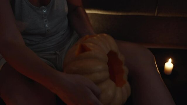 A girl by candlelight in a red light admires a carved pumpkin for Halloween.