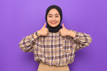 Cheerful young Asian woman in plaid shirt showing thumbs up isolated on purple background