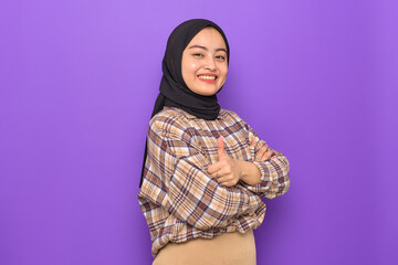 Cheerful young Asian woman in plaid shirt showing thumbs up isolated on purple background