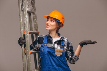 Repair woman standing by the  ladder wearing overalls uniform and holding painting brush