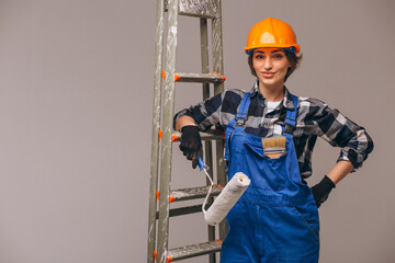 Repair woman standing by the  ladder wearing overalls uniform and holding painting brush