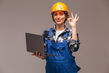Repair woman in hard hat and overalls holding laptop