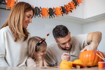 Happy family carving pumpkin for Halloween holiday together, preparing for holiday party in kitchen.