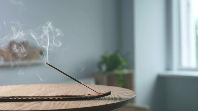 Holder with smoldering incense stick on wooden table in room