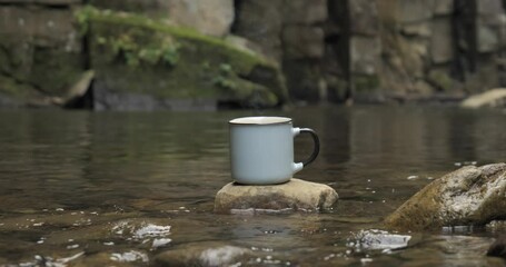 A mug on a stone near a fire on the river bank