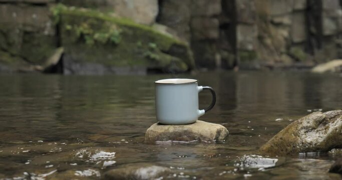 A mug on a stone near a fire on the river bank