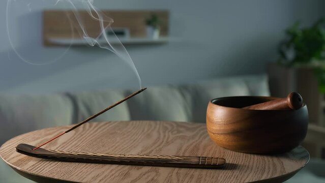 Holder with smoldering incense stick on wooden table in room