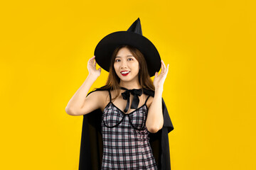 Young asian woman wearing witch hat and witchcraft and black dress posing on yellow color...