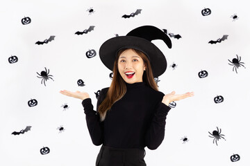 Halloween concept, young asian woman in black costume wearing witch hat and holding pumpkin lantern posing on graphic black and white background.