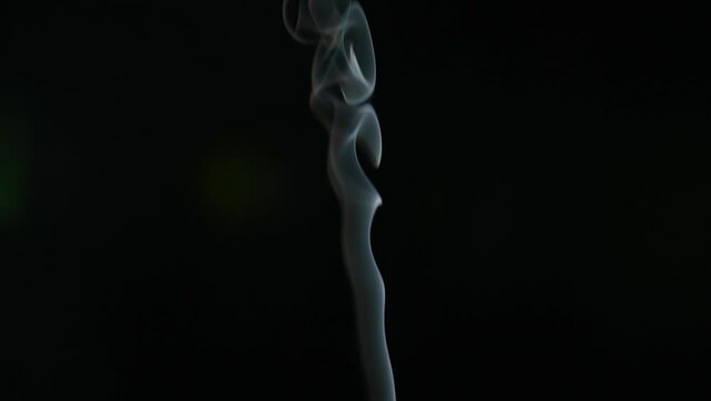 White smoke from incense stick flowing on black background