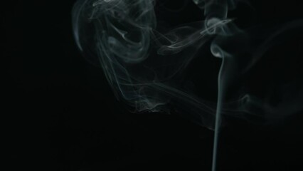 White smoke from incense stick flowing on black background
