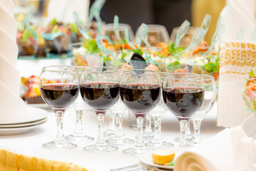 Glasses of red wine, delicacies, snacks and desserts on luxuriously served buffet tables. Restaurant business, catering.
