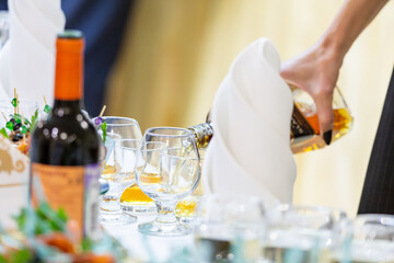 The waiter pours whiskey or cognac into a glass. Buffet tables at the event.
