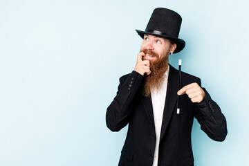 Young magician man isolated on blue background relaxed thinking about something looking at a copy space.