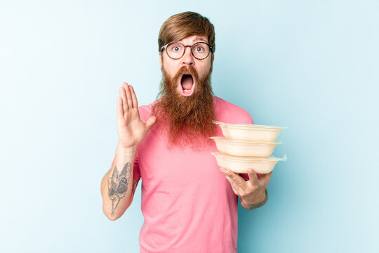 Young caucasian man holding a tupper ware isolated on blue background surprised and shocked.