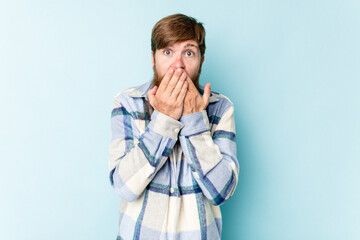 Young caucasian red-haired man isolated on blue background shocked, covering mouth with hands, anxious to discover something new.