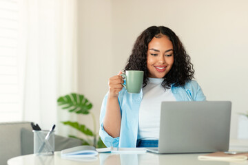 Black Female Using Laptop Drinking Coffee Working Online In Office