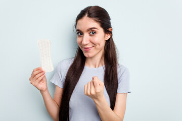 Young caucasian woman holding a sanitary napkin isolated on blue background pointing with finger at you as if inviting come closer.