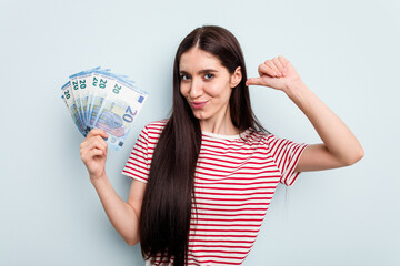 Young caucasian woman holding banknotes isolated on blue background feels proud and self confident, example to follow.