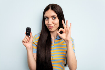 Young caucasian woman holding car keys isolated on blue background cheerful and confident showing ok gesture.