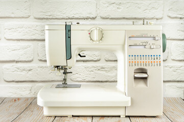 Modern multi operation sewing machine, assortment of different stitches for decorating clothes on table in tailor's workshop or atelier on white brick background.