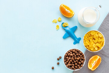 Kids breakfast with corn flakes, milk and orange, top view