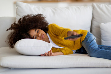 Bored black school girl lying on couch, watching TV