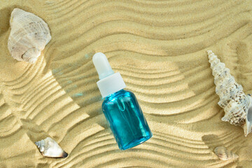 A glass jar with essential oil lies on the sand. Skin care products and sun protection