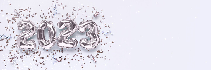 Banner with 2023 silver foil inflatable balloons, stars confetti and ribbons on a blue background. New Year's concept with copy space.