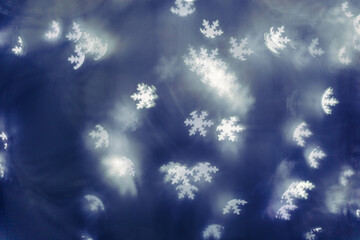 White snowflakes bokeh lights on blue background, abstract winter holiday wallpaper with optical blurred glittering pattern. Christmas or New Year abstract composition as backdrop, monochrome