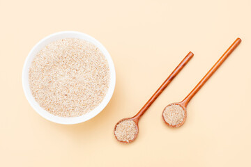 Wooden spoon and bowl with psyllium husk close-up on brown background.