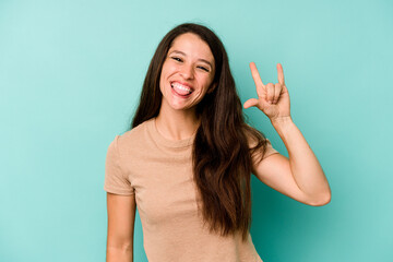 Young caucasian woman isolated on blue background showing a horns gesture as a revolution concept.