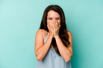 Young caucasian woman isolated on blue background laughing about something, covering mouth with hands.