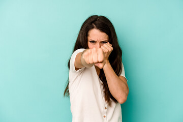 Young caucasian woman isolated on blue background throwing a punch, anger, fighting due to an...