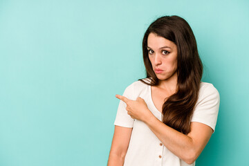 Young caucasian woman isolated on blue background smiling and pointing aside, showing something at blank space.