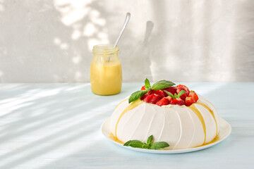 Pavlova cake with strawberries and lemon curd on a light sunny background.