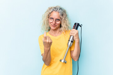 Middle age woman holding a blender isolated on blue background pointing with finger at you as if inviting come closer.