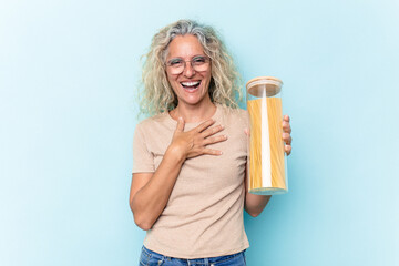 Middle age caucasian woman holding a spaghettis jar isolated on blue background laughs out loudly keeping hand on chest.
