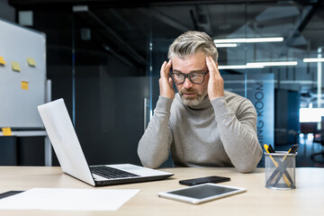 Sick mature businessman working in modern office, senior experienced man having severe headache,...
