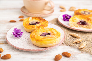 Small cheesecakes with jam and almonds with cup of coffee on a white wooden background. Side view, selective focus.