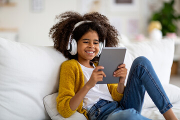 Happy kid sitting on couch, using digital tablet and headset