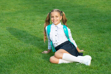 Fototapeta premium Happy teen girl in school uniform sitting on green grass. Teenage girl back to school. September 1