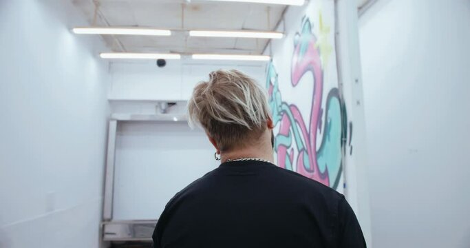 A graffiti artist looks at his work in a contemporary art gallery. Handheld camera