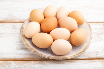 Pile of colored eggs on plate on a white wooden background. side view.