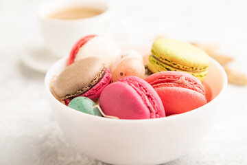 Different colors macaroons and chocolate eggs in ceramic bowl, cup of coffee on gray concrete background. side view, close up.