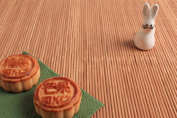 Chinese moon cake and the rabbit is a symbol of autumn on a bamboo mat background. Asian traditional mid-autumn festival. Translation of hieroglyphs: mango, pomegranate and lotus